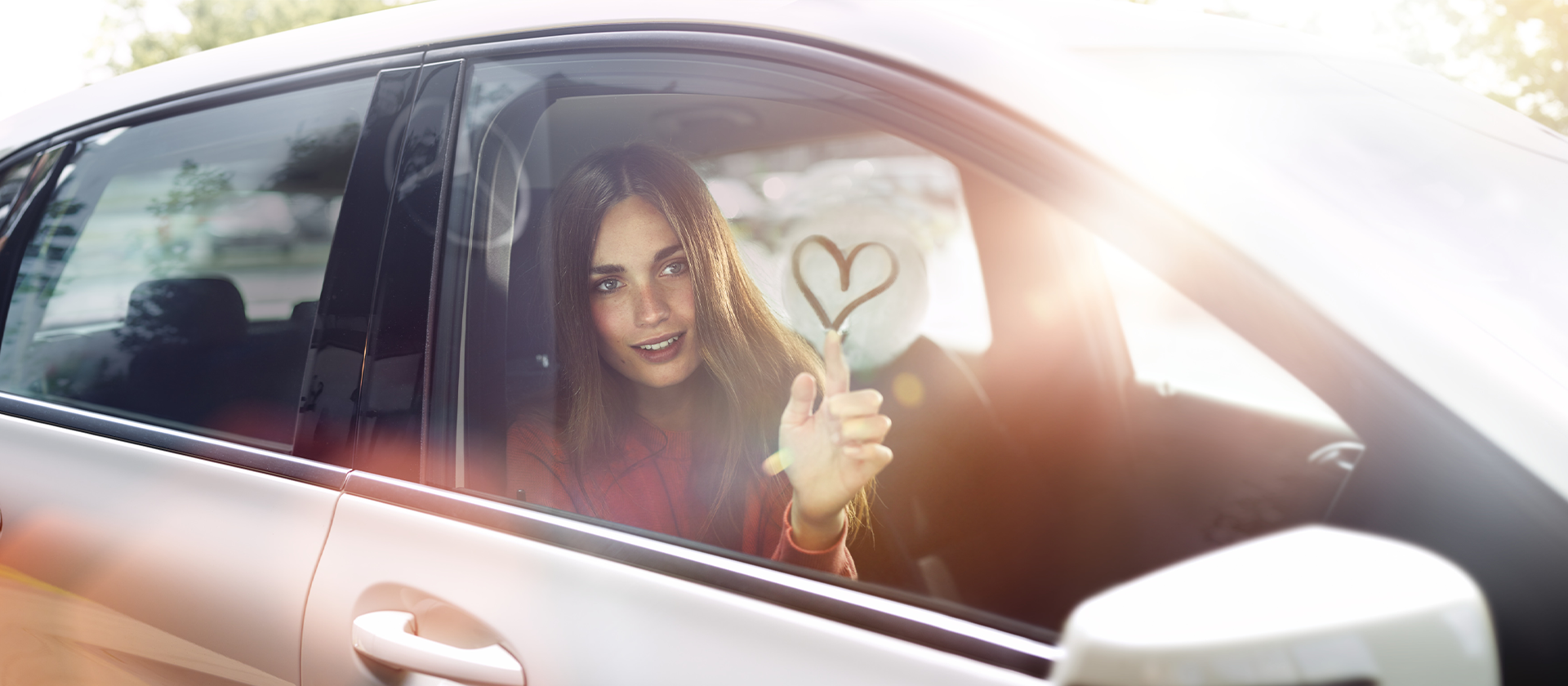 Eine Frau im Auto malt an feuchte Scheibe ein Herz